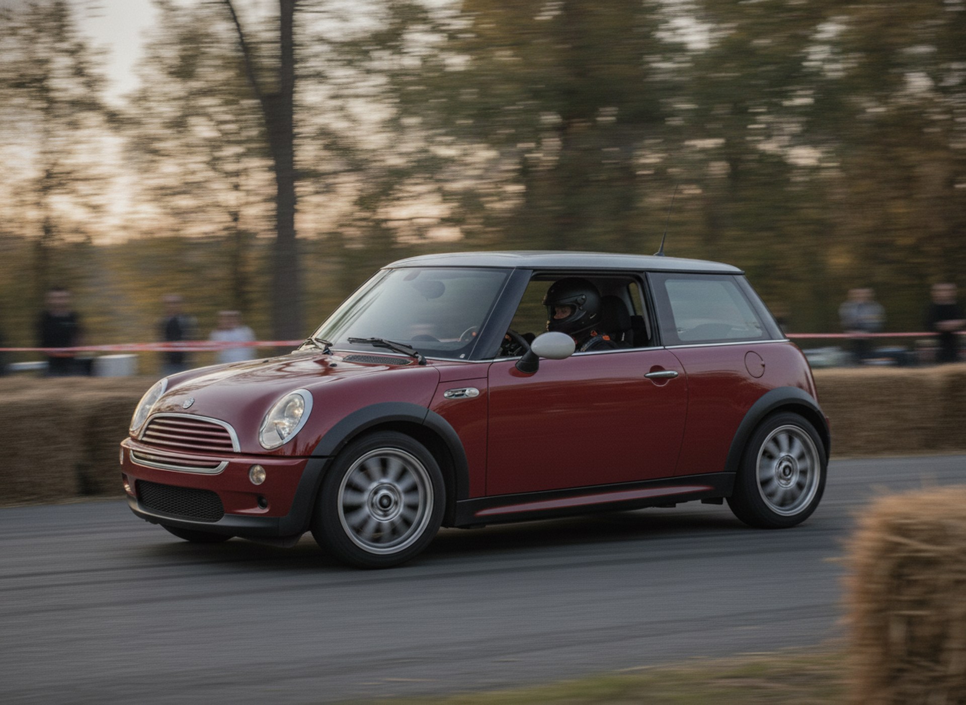 Red BMW Mini One R50 being driven hard through a corner on a tarmac rally stage, driver in a plain black helmet