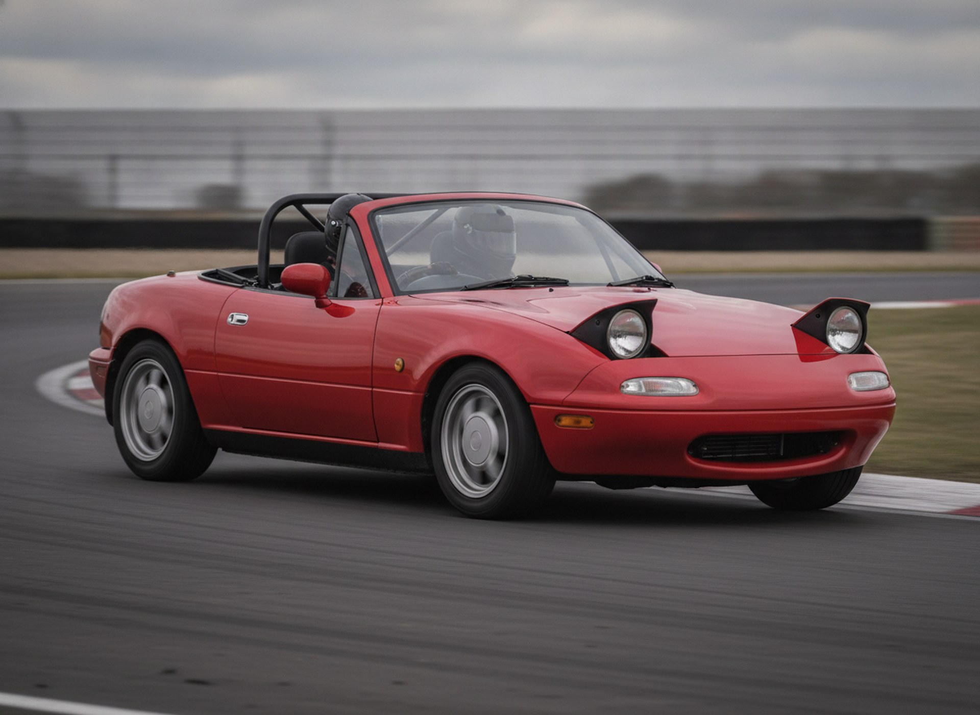 Red Mazda MX5 Mk1 on a race circuit, driver in a plain black helmet, big brake kit guide