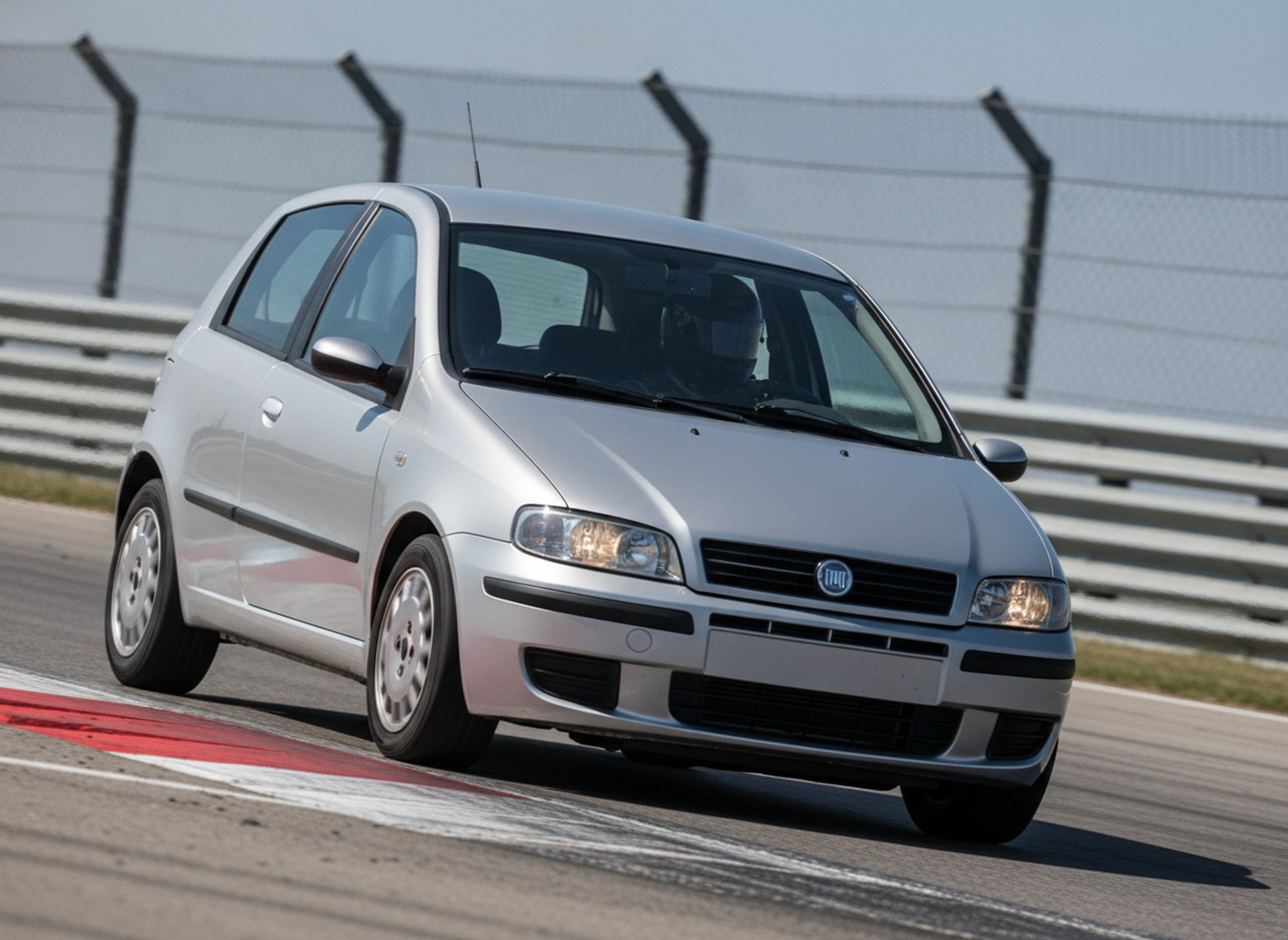 Silver Fiat Punto MK2 on track with driver in black helmet