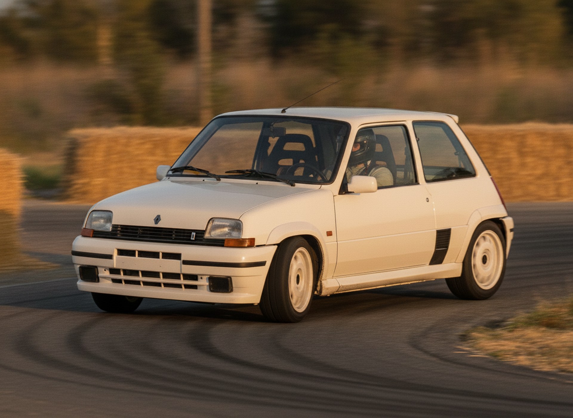 White Renault 5 GT Turbo driven hard through a corner on a rally stage, driver in a plain black helmet