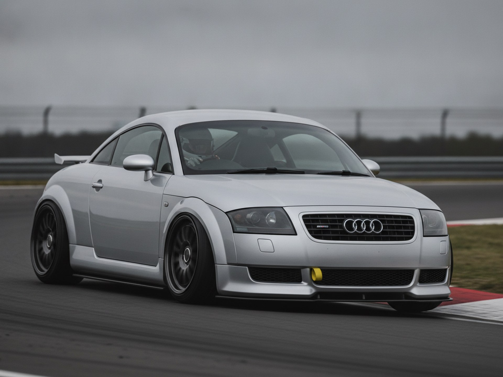 Silver Audi TT 8N coupe on a race circuit, driver in a plain black helmet, big brake kit guide