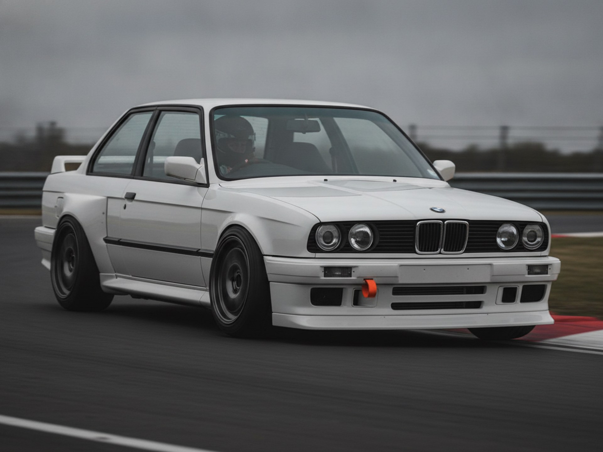 White BMW E30 3-Series being driven hard through a corner on a race circuit