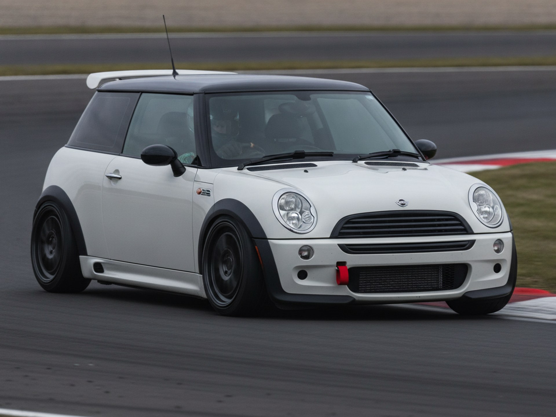 Red BMW Mini One R50 being driven hard through a corner on a tarmac rally stage, driver in a plain black helmet