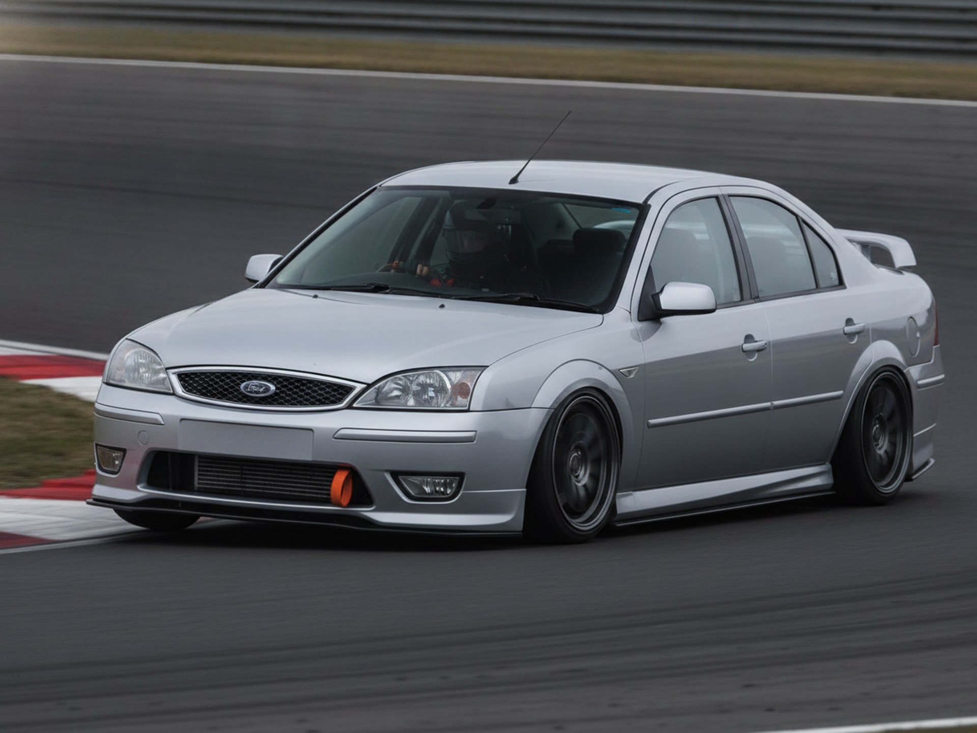 Blue Ford Mondeo MK3 saloon on a race circuit, driver in plain black full-face helmet, big brake kit guide