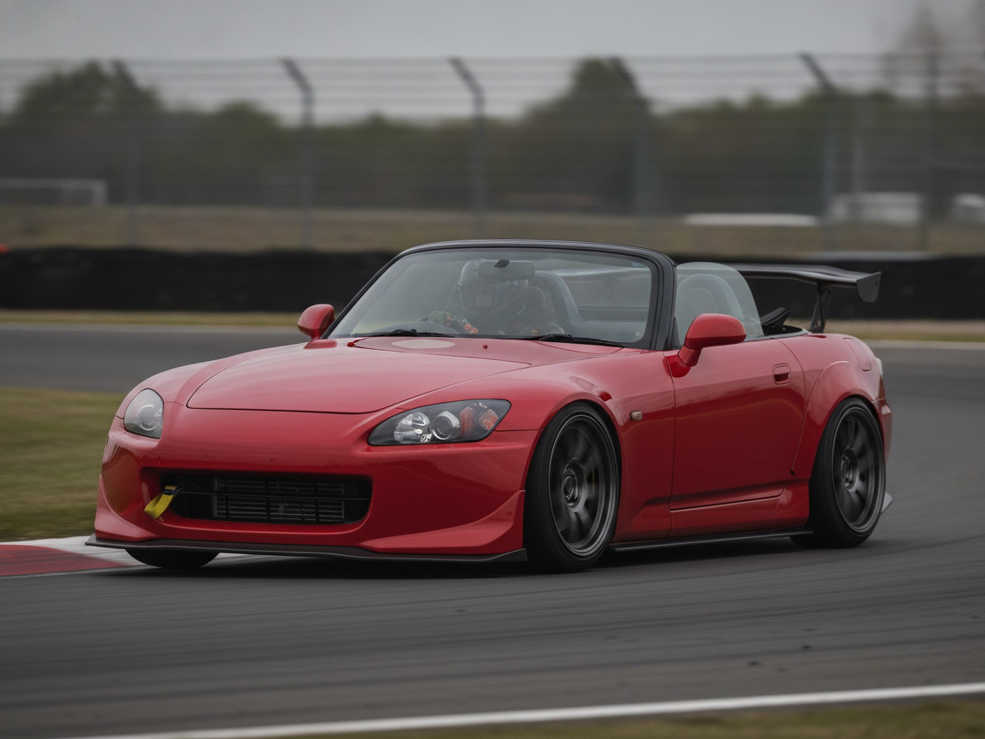 Red Honda S2000 roadster being driven hard through a corner on a race circuit