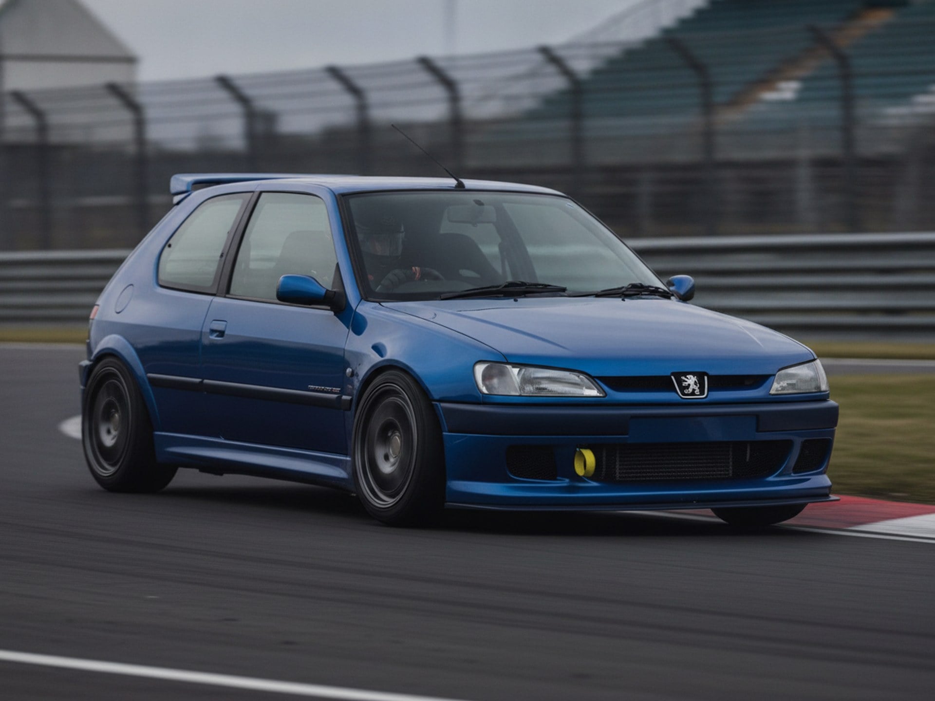 Blue Peugeot 306 GTI-6 being driven hard through a corner on a rally stage, driver in a plain black helmet