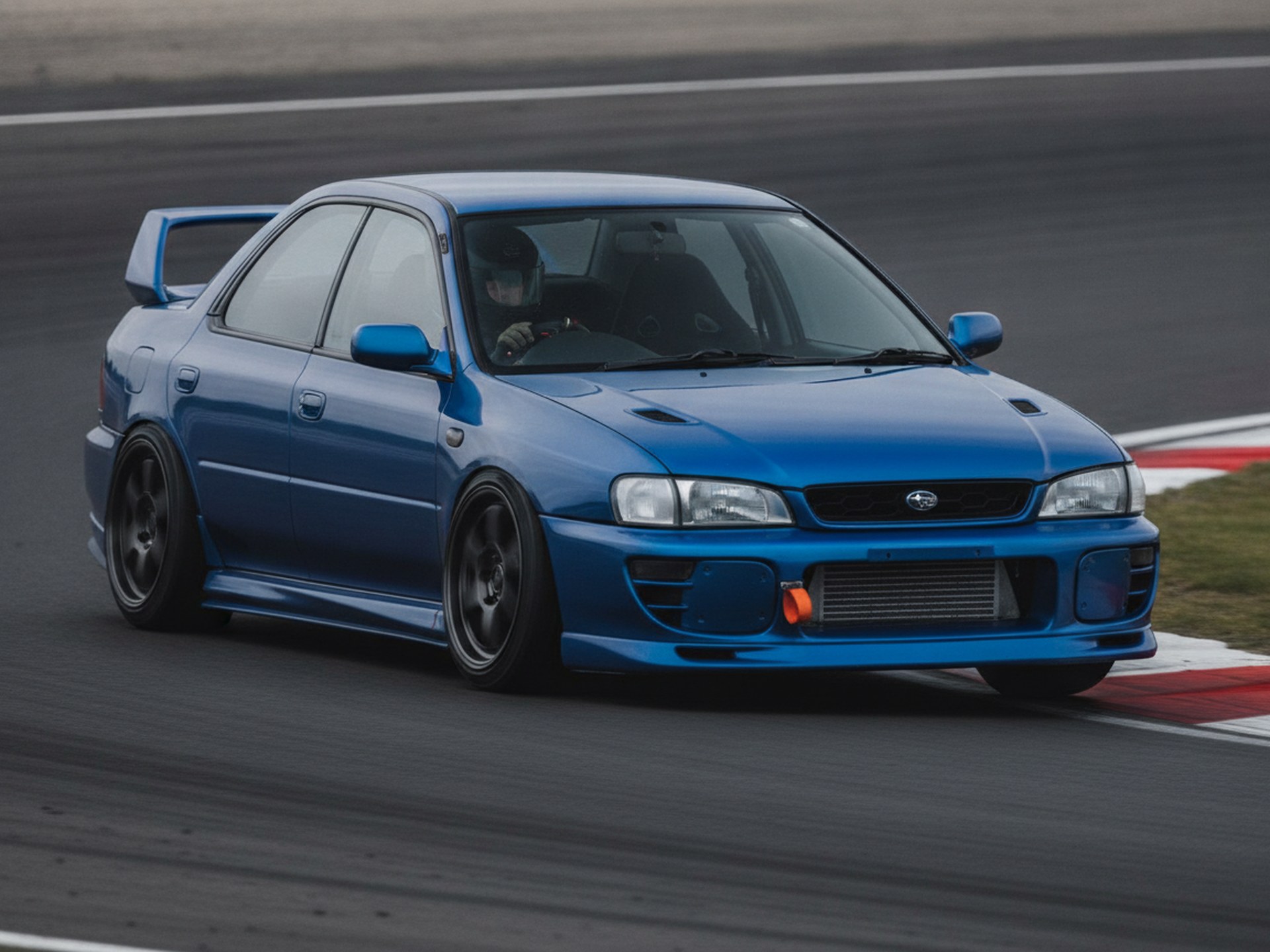 Modified Subaru Impreza on a race circuit, driver in a plain black helmet